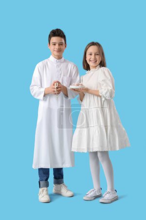 Cute Muslim kids with traditional sweets on blue background. Eid al-Fitr celebration