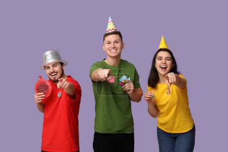 Young friends in funny disguise with paper fishes and whoopee cushion on purple background. April fool's day celebration