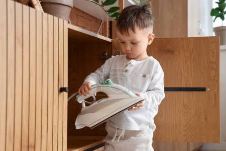 Little boy taking electric iron from drawer at home. Child in danger