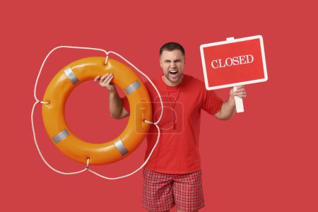 Shouting young lifeguard with lifebuoy and sign "closed" on red background