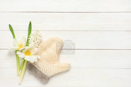 Massagehandschuh und Blumen auf hellem Holzhintergrund