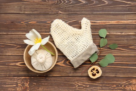 Komposition mit Massagehandschuh, Kräuterbeutel und Blume auf Holzgrund