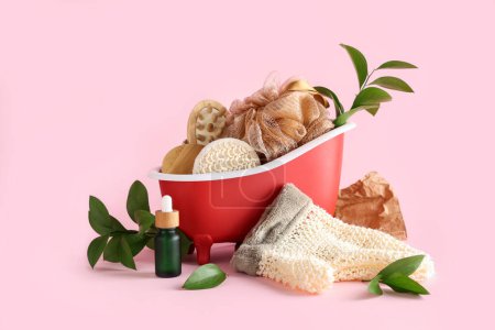 Komposition mit Mini-Badewanne, Wellness-Accessoires und Pflanzenzweigen auf rosa Hintergrund