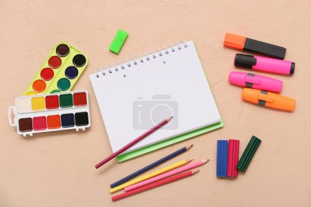 Foto de Cuaderno, lápices de colores y acuarelas sobre fondo beige. Vista superior - Imagen libre de derechos