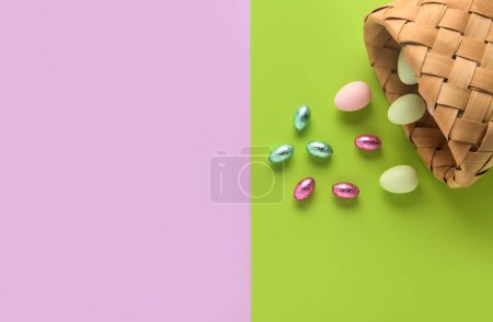 Téléchargez les photos : Panier renversé avec oeufs de Pâques peints et bonbons sur fond de couleur - en image libre de droit
