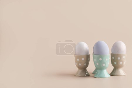 Ceramic holders with Easter eggs on beige background