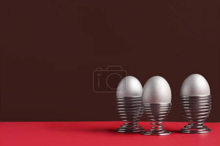 Painted eggs in egg holders on red table against brown background