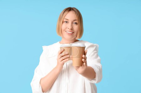 Téléchargez les photos : Heureuse femme adulte avec des tasses en papier de café sur fond bleu - en image libre de droit