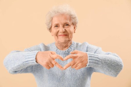 Femme âgée faisant coeur avec ses mains sur fond beige