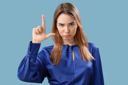 Upset young woman showing loser gesture on blue background