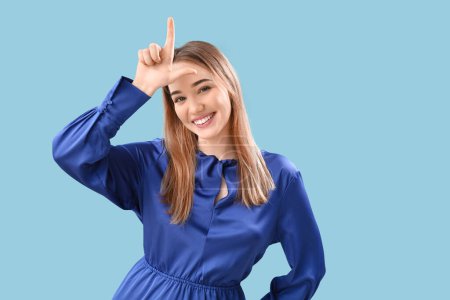 Young woman showing loser gesture on blue background