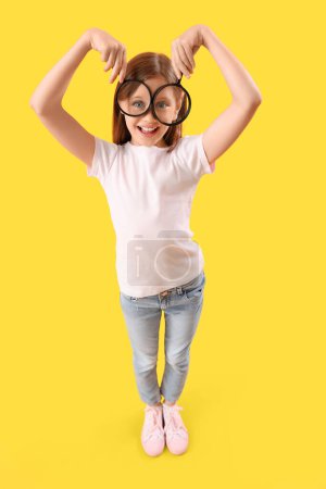 Funny little girl with magnifiers on yellow background
