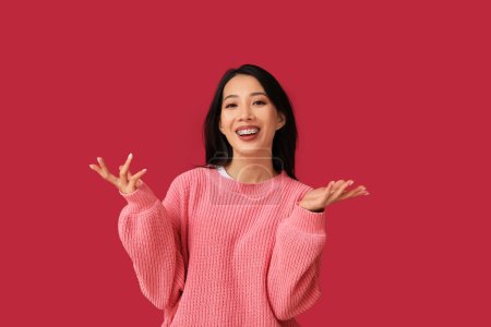 Young Asian woman laughing on red background