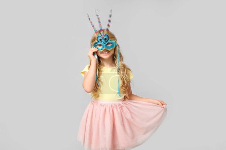 Photo for Adorable little girl wearing carnival mask on light background - Royalty Free Image
