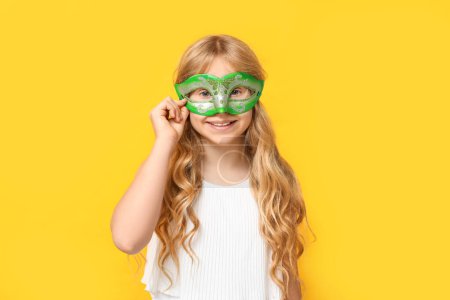 Photo for Happy little girl wearing carnival mask on yellow background - Royalty Free Image