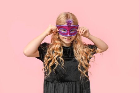 Happy little girl wearing carnival mask on pink background