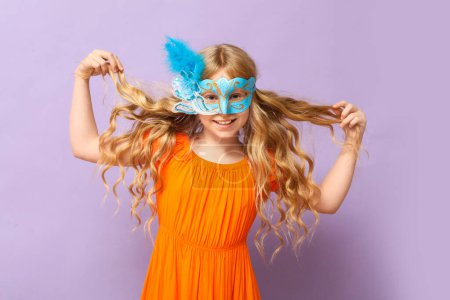 Photo for Adorable little girl wearing carnival mask on lilac background - Royalty Free Image