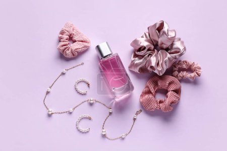Bottle of perfume with earrings, necklace and scrunchies on lilac background