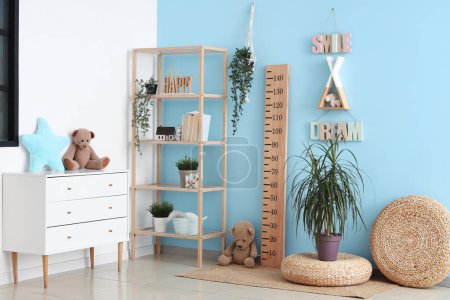 Interior of stylish children's room with wooden stadiometer, chest of drawers and toys