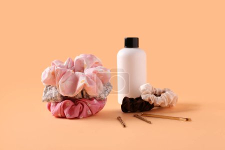 Bottle of cosmetic product with scrunchies and hairpins on orange background