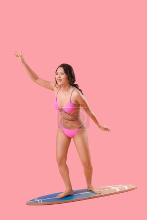 Sexy young woman on surfboard against pink background
