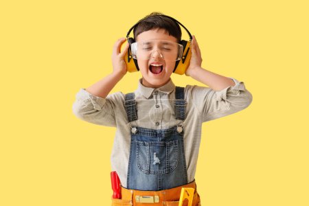 Foto de Lindo pequeño constructor en protectores auditivos gritando sobre fondo amarillo - Imagen libre de derechos