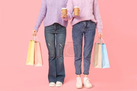 Téléchargez les photos : Jeunes sœurs avec des tasses en papier de café et des sacs à provisions sur fond rose - en image libre de droit