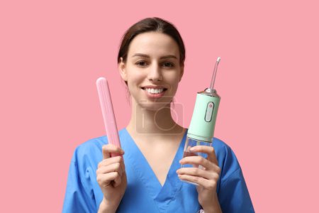 Téléchargez les photos : Dentiste féminine avec irrigateur oral et étui sur fond rose - en image libre de droit