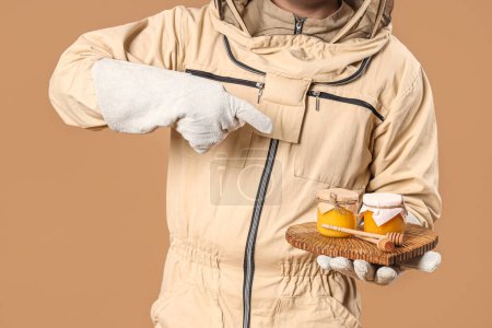 Male beekeeper pointing at honey on brown background, closeup