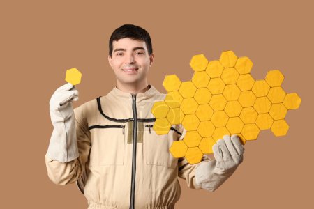 Male beekeeper with paper honeycombs on brown background