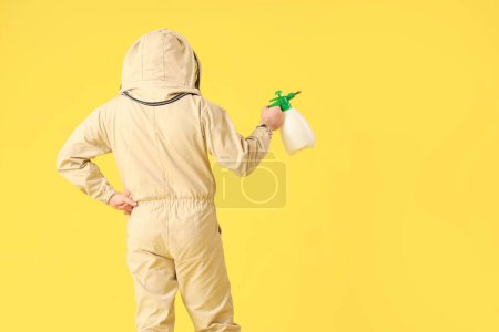 Male beekeeper with sprayer on yellow background, back view