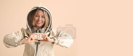 Female beekeeper showing heart gesture on beige background with space for text