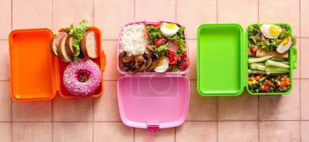 Foto de Loncheras con diferentes sabrosos alimentos sobre fondo de baldosas de color rosa - Imagen libre de derechos