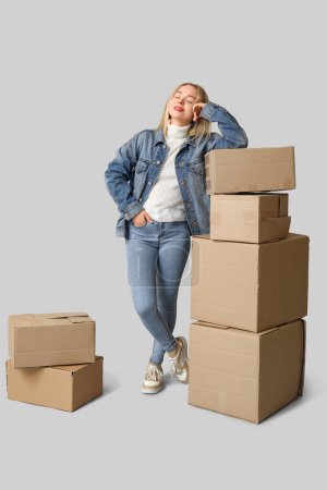 Foto de Mujer joven feliz con cajas de cartón sobre fondo gris. Mudarse a un nuevo concepto de casa - Imagen libre de derechos