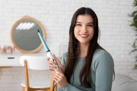 Photo for Beautiful young happy woman with curling iron at house - Royalty Free Image