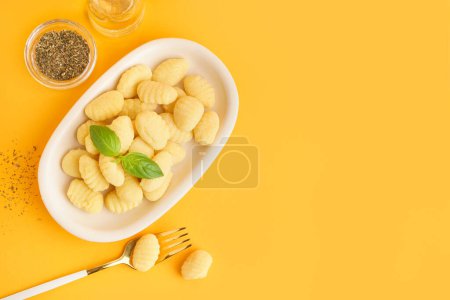 Plate with tasty gnocchi, basil, spices and fork on orange background