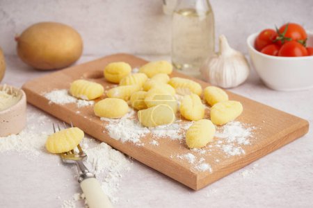 Wooden board with tasty gnocchi and fork on light background, closeup
