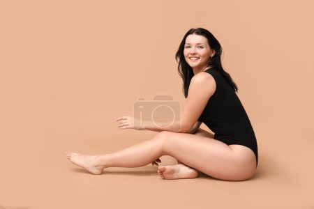 Body positive young woman sitting on beige background