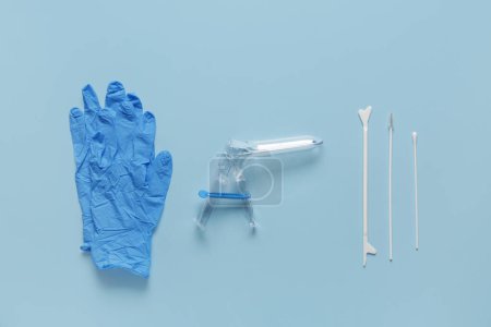 Gants médicaux avec spéculum gynécologique et outils de test de frottis de pap sur fond bleu