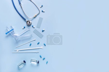 Stethoskop mit gynäkologischem Spekulum, Pap-Abstrichtestgeräten und Pillen auf blauem Hintergrund