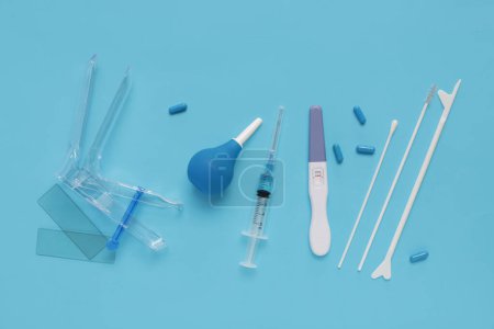 Speculum gynécologique avec des outils de test de frottis de pap, test de grossesse et lavement sur fond bleu