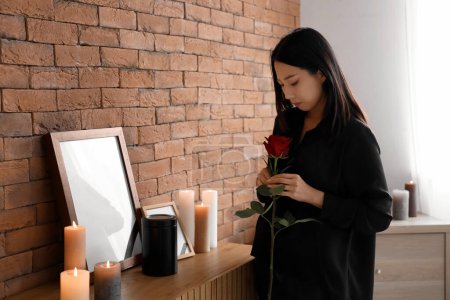 Dolor joven mujer asiática con rosa y urna funeraria en el funeral