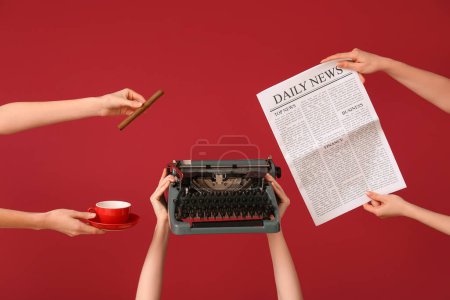 Manos femeninas sosteniendo periódico con máquina de escribir vintage, cigarro y taza de café sobre fondo rojo