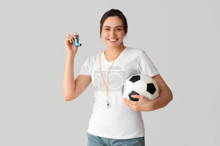 Sporty young woman with soccer ball and inhaler on light background