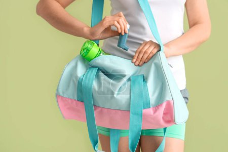 Sporty young woman with inhaler and bag on green background, closeup