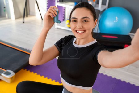 Sportliche junge Frau mit Inhalator macht Selfie im Fitnessstudio