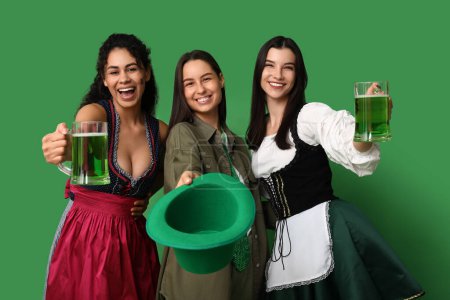 Téléchargez les photos : Belles jeunes femmes avec des verres de bière sur fond vert. Célébration de la Saint Patrick - en image libre de droit