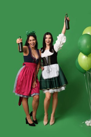 Camareras irlandesas con botellas de cerveza y globos aéreos sobre fondo verde. Celebración del Día de San Patricio