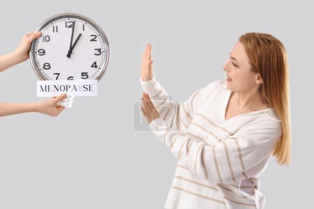 Mature woman rejecting clock and suppositories on light background. Menopause concept