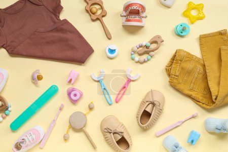 Téléchargez les photos : Vêtements bébé avec brosses à dents, modèle à mâchoires et jouets sur fond beige - en image libre de droit